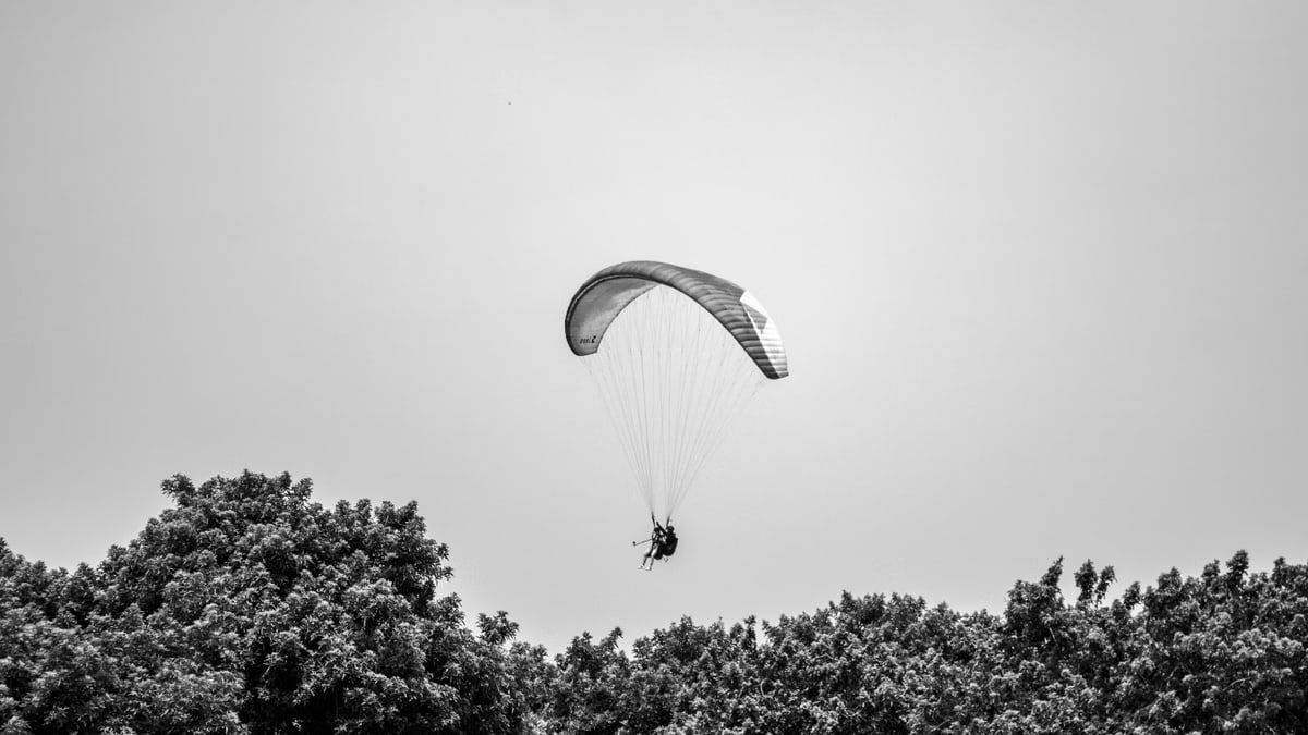 A paraglider gracefully glides above the lush trees in Lima, Peru, under a cloudless sky.